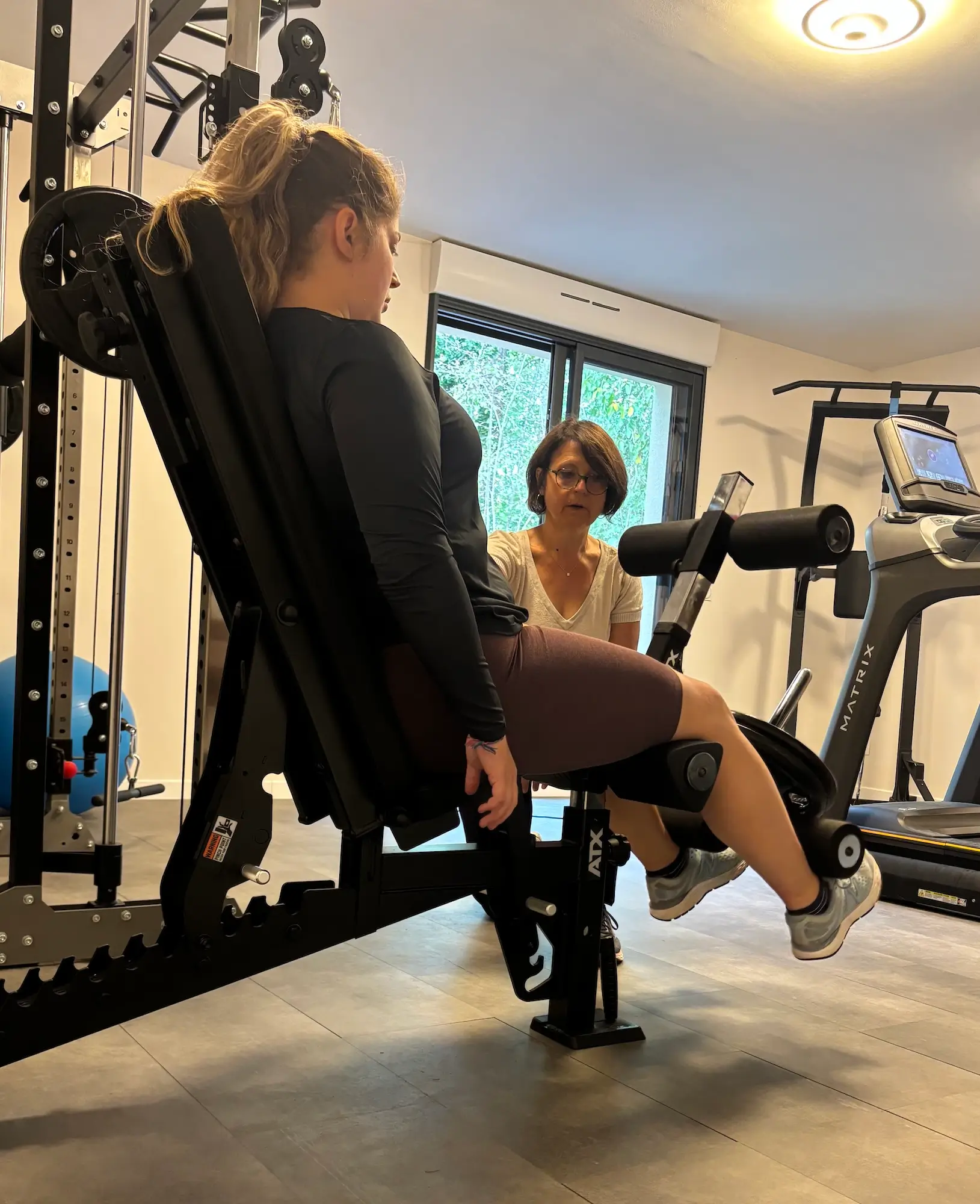 La coach corrige la posture d'une cliente sur machine leg extension en séance individuelle