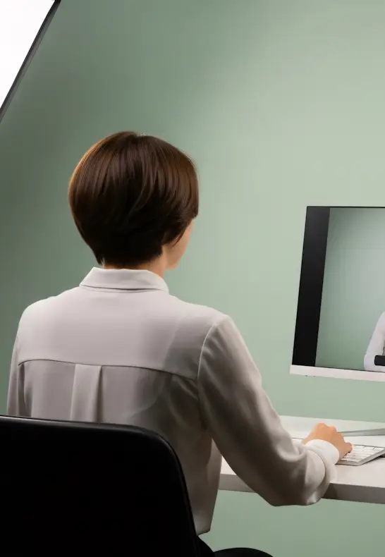 Femme de dos en visioconférence devant un écran d'ordinateur, pour une séance de coaching ergonomie au travail